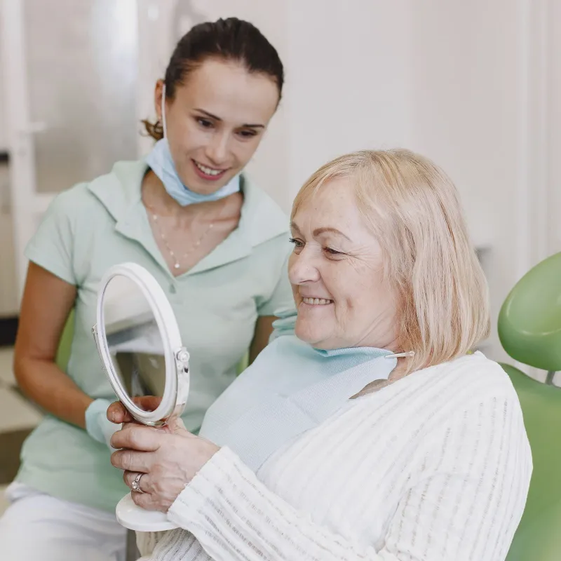Smiling senior patient checking her smile in a mirror with a dentist